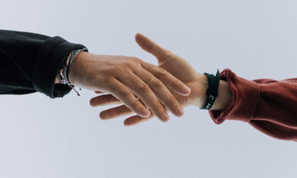 Two individuals shaking hands against a clear blue sky, symbolizing agreement and collaboration.