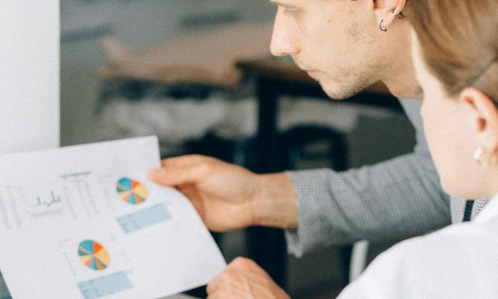 A man and woman analyze a chart displayed on a computer screen, engaged in discussion and collaboration.